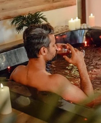 Gost uživa v topli mineralni kopeli s kozarcem vina ob svečah
